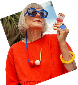 A person wearing large sunglasses and a red top holding an ice cream.