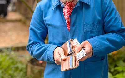 A person holding a wallet while offering banknotes in a garden setting.